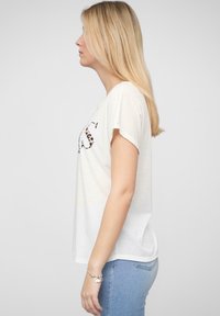 T-shirt blanche à manches courtes avec une lettre "S" en imprimé léopard sur le devant, associée à un jean bleu ajusté. Tissu doux et léger.