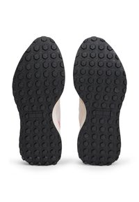 Αθλητικά παπούτσια με μπεζ πάνω μέρος και μαύρη εξαγωνική εξωτερική σόλα από καουτσούκ. Σημαντικές ροζ λεπτομέρειες στις πλευρές, με ορατή λεπτομέρεια επωνυμίας.