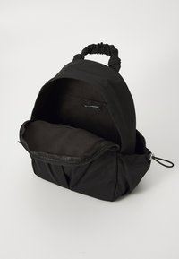Black fabric backpack with a soft texture, rounded shape, cinched handle, and a zippered compartment. Interior lined in dark fabric.