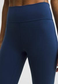 Marinblå högmidjade leggings tillverkade av ett mjukt, stretchigt tyg med platta sömmar. Har en bred midja och inget synligt mönster.