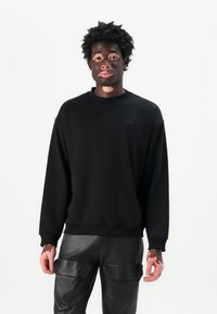 Sweatshirt noir avec un col ras du cou et des manches longues, affichant un logo discret. Associé à un pantalon cargo noir avec des poches.