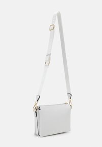 Bílá kožená crossbody taška s obdélníkovým tvarem, zlatými kovovými prvky a texturovaným povrchem. Obsahuje nastavitelný popruh s logem.