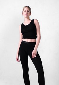 Sort tætsiddende tanktop og leggings lavet af et glat, strækbart stof. Toppen har en rund halsudskæring, og leggingsne har en høj talje.