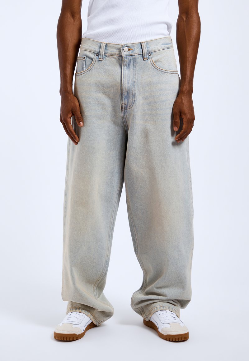 Jasnoniebieskie dżinsy o luźnym kroju, z wysokim stanem, subtelnymi przetarciami i przeszyciami. Noszone z białymi trampkami.