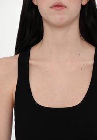 Débardeur noir côtelé avec des bretelles larges et un col arrondi, mettant en valeur une texture lisse contre la peau nue. Détails visibles minimaux.