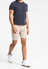 Granatowa koszulka z krótkim rękawem w białe kropki, połączona z beżowymi szortami. Model nosi białe sneakersy z czarnymi akcentami i gumową podeszwą.