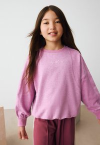 Helles pinkes Sweatshirt mit geripptem Halsausschnitt und Bündchen, versehen mit "Sports Club" in weißer Stickerei, kombiniert mit bordeauxroten Hosen mit weißen Streifen.
