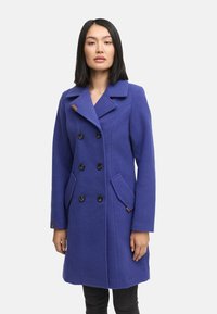 Purple wool double-breasted coat featuring two large front pockets, black buttons, and a notched collar. Accented with a brown detail on the lapel.