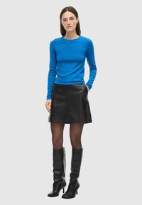 Blå langermet strikket topp kombinert med et svart skinn A-linje skjørt, svarte knelangt støvler med hæl, og en jevn tekstur gjennom hele antrekket.