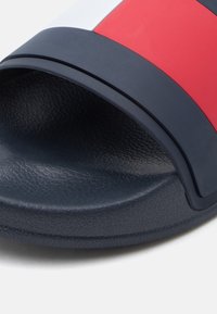 Μαύρο σανδάλι με λαστιχένια σόλα με υφή, διακοσμημένο με οριζόντιες κόκκινες, λευκές και μπλε ρίγες στο πάνω λουρί.