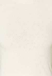 Vit stickad tröja med en texturerad yta, rund halsringning och subtila fläckade detaljer genom tyget.