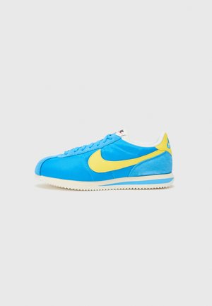 Zapatillas Nike en azul y amarillo con parte superior de ante y sintético, con puntera redondeada, suela blanca y logo swoosh prominente.