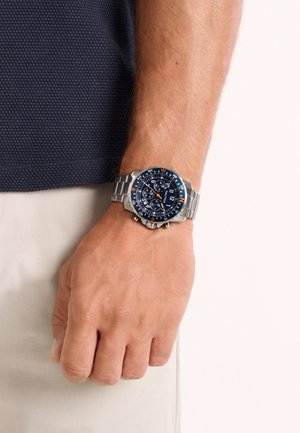 Roostevabast terasest käekell sinise sihverplaadi, mitme abiketta ja oranžide aktsentidega. Omab metallist rihma ja silmatorkavat raamiga, millel on põhisuunad.