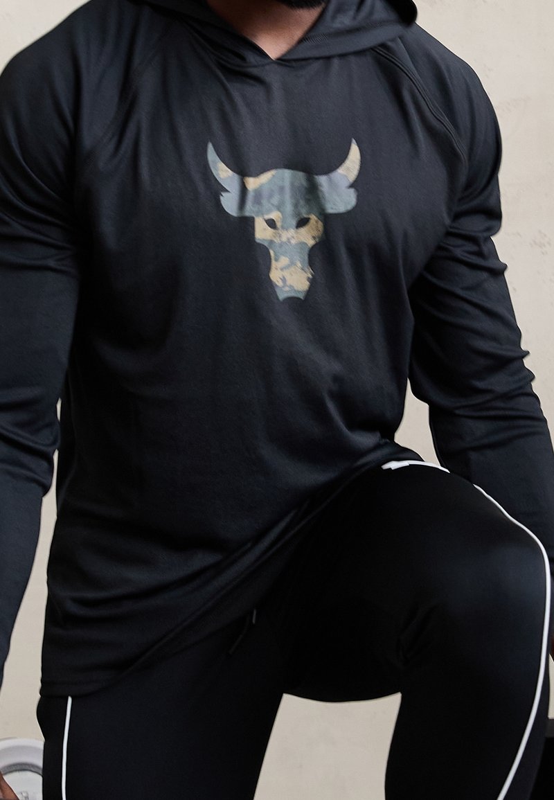 Schwarzer Langarm-Hoodie mit einem Camouflage-Bullenkopf-Graphic auf der Brust. Hat eine entspannte Passform und eine weiche Textur, getragen mit schwarzen Sporthosen.