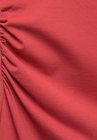 Tissu texturé corail avec de doux plis froncés, créant une apparence lisse et fluide avec un motif légèrement nervuré.