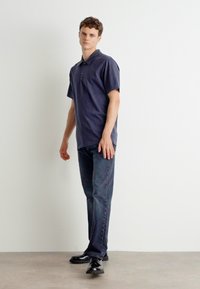 Granatowa koszulka polo z krótkim rękawem, w połączeniu z ciemnymi dżinsami i czarnymi butami eleganckimi. Prosty design, minimalne detale i gładka faktura.