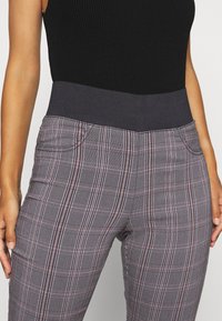 Pantalones de cuadros grises con una cinturilla ancha y elástica de color oscuro y bolsillos laterales, fabricados con un tejido suave. Se pueden ver acentos rojos y negros.