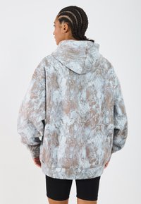 Prehnaný mikina v mnohobarevnej šedej a hnedej mramorovej vzore, s veľkou kapucňou a mäkkou, štruktúrovanou tkaninou. Navrhnutý pre pohodlie.