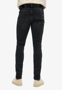 Jeans ajustados de mezclilla oscura con una cintura de altura media, que cuentan con dos bolsillos traseros y un acabado limpio. Combinados con zapatillas de color claro.