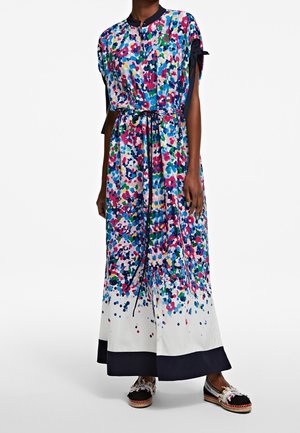 Mujer con vestido maxi floral de colores con cintura entallada y ribete negro, combinado con alpargatas negras y blancas.