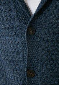 Cárdigan de punto en color navy con un patrón de zigzag texturizado, cuello con muesca y cierre de botón oscuro. Tejido suave con fibras visibles.