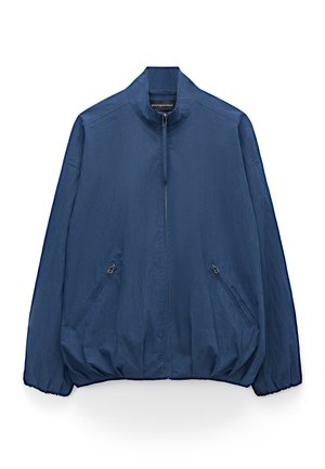 Veste légère bleu marine avec col montant, fermeture éclair frontale, deux poches latérales zippées, poignets et ourlet élastiqués.