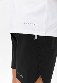Hvit treningsskjorte med "Morotai"-merke, kombinert med svarte shorts som har reflekterende detaljer, sidelommer og perforerte aksenter.