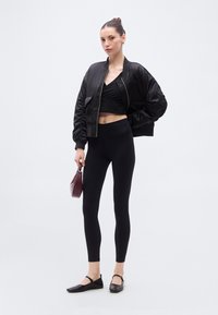 Μαύρο σατινέ bomber τζάκετ, cropped τοπ, μαύρο legging ψηλόμεσο και μαύρα φλατ παπούτσια. Τα αξεσουάρ περιλαμβάνουν μια μικρή μπορντό τσάντα.