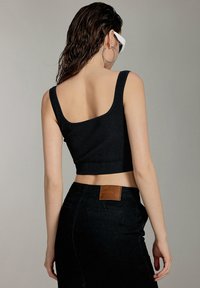 Top corto nero a coste con spalline larghe, abbinato a una gonna nera a vita alta con una toppa in pelle marrone sul retro.