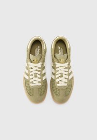 Grønne sneakers med vævet tekstil og ruskind, med tre hvide striber, gyldne accenter og en gummisål.