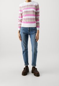 Stickad tröja med rosa, vit och beige zick-zack-mönster. Ribbad fåll och ärmslut. Bärs med ljusblå jeans och bruna slip-on skor.