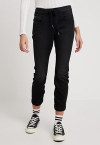 Svarta joggerbyxor med elastiskt midjeband, framfickor, manschetter och en mjuk textur, tillsammans med svart-vita sneakers.