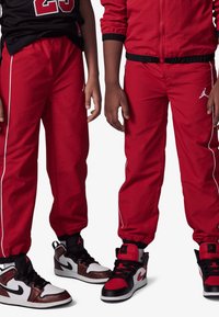 Rote Baumwoll-Trainingshose mit weißen Seitenstreifen und Jordan-Logo, kombiniert mit schwarzen und roten High-Top-Sneakern mit einzigartigen Akzenten.