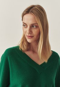 Grüner, strukturierter Pullover mit V-Ausschnitt. Das weiche Material verstärkt die lässige Passform und weist ein dezentes Nahtdetail am Halsausschnitt auf.