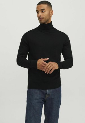 Suéter negro de cuello alto en tejido suave, con mangas largas y puños acanalados. Combinado con jeans oscuros.