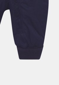 Marineblauwe gewatteerde broek met geribde boorden, voorzien van een zijzak met rits en een zachte textuur. Het ontwerp bevat ronde stikpatronen.