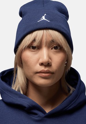 Beanie a maglia color navy con il logo Jumpman bianco sulla parte anteriore. Modello che indossa una felpa navy coordinata. Texture morbida e design leggermente sformato.