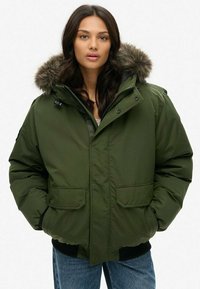 Green puffer jacket with a fur-lined hood, two front pockets, and a front zipper. Features a thick, textured fabric and ribbed cuffs.