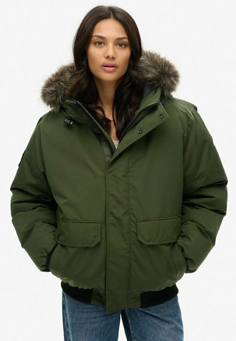 Green puffer jacket with a fur-lined hood, two front pockets, and a front zipper. Features a thick, textured fabric and ribbed cuffs.