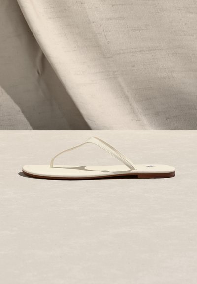 Μίνιμαλ μπεζ σανδάλι σφήνα με λεπτά λουράκια και επίπεδη σόλα σε ανοιχτή υφή επιφάνεια και φόντο από ύφασμα.