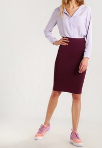 Blusa morada de manga larga con un bolsillo, falda lápiz burdeos ajustada y zapatillas en tonos pastel rosa y blanca. Tela suave, corte entallado.