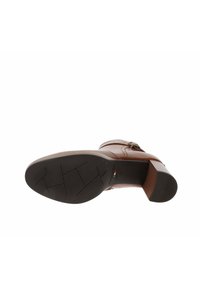 Chaussure en cuir marron avec une surface lisse, un bout arrondi et un petit talon bloc. La semelle présente un motif texturé pour l'adhérence.