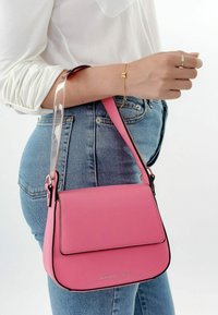 Bolso de mano rosa hecho de material suave, con un ribete negro, cierre tipo solapa y una correa transparente. El diseño es compacto y rectangular.