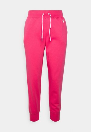 Pantalon de survêtement rose vif avec cordon blanc et petit logo blanc brodé sur le côté supérieur gauche, sur un fond gris clair uni.