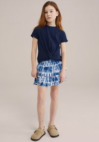 Tricou bleumarin legat la gât, fustă tiered cu tie-dye albastru și saboți bej. Material neted, design casual, mâneci scurte și detaliu cu talie strânsă.