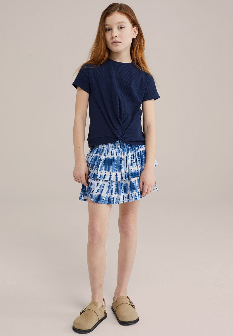 Tricou bleumarin legat la gât, fustă tiered cu tie-dye albastru și saboți bej. Material neted, design casual, mâneci scurte și detaliu cu talie strânsă.