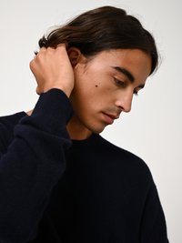 Marineblauer Pullover aus weichem Stoff, mit rundem Ausschnitt und langen Ärmeln. Die Person hat lange, sanft gestylte Haare.