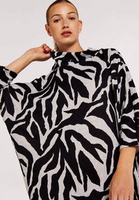 Schwarzes und graues übergroßes Oberteil mit Zebra-Streifen-Muster, aus weichem Stoff mit hohem Kragen und weiten Ärmeln.