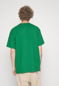 Camiseta de algodón verde con un corte relajado, cuello redondo y mangas cortas, con un diseño liso y sin adornos visibles.
