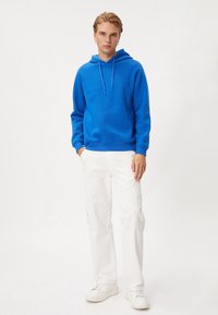 Blå bomullshoodie med dragsko, kombinerad med vita cargobyxor och vita sneakers. Outfiten har en avslappnad passform och mjuk textur.